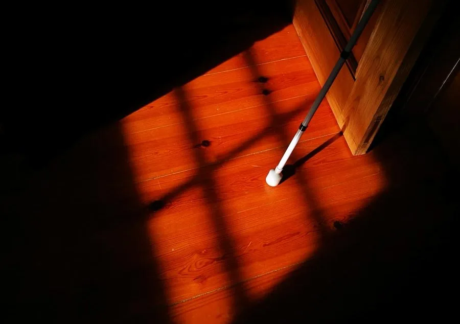 Imagem ilustrativa do projeto com uma bengala de invisual encostada a uma porta nas sombras.